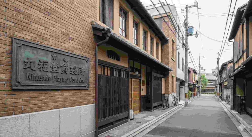 A photograph of the exterior of the former Nintendo headquarters building in Kyoto, now the Marufukuro hotel, featuring the original historic plaque reading "Nintendo Playing Card Co."