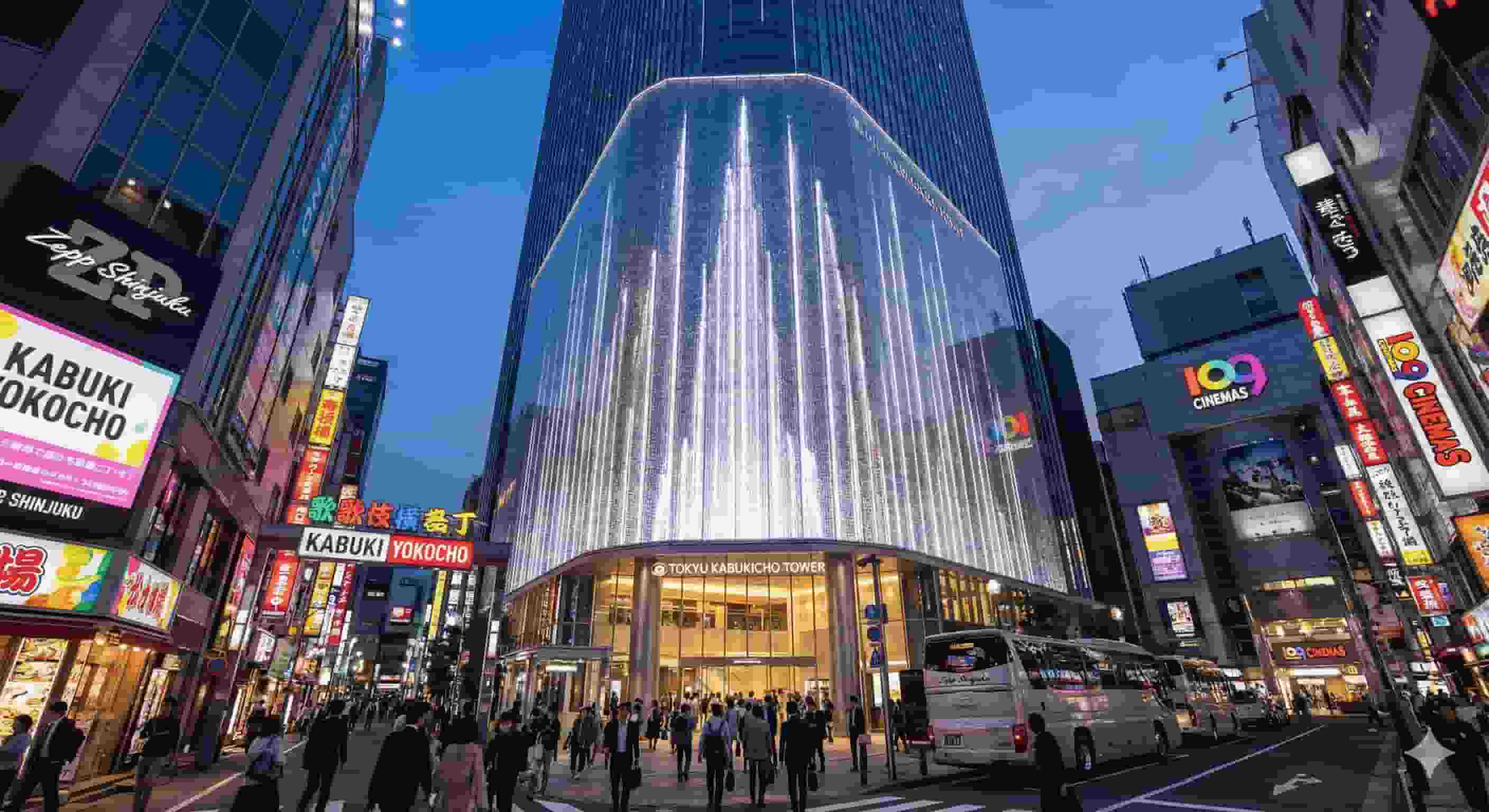 The illuminated exterior of Tokyu Kabukicho Tower at night in Shinjuku, showcasing the fountain-inspired architecture and neon signs for Kabuki Yokocho and Zepp Shinjuku.